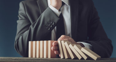 Front view of successful business crisis manager stopping collapsing dominos in a conceptual image.