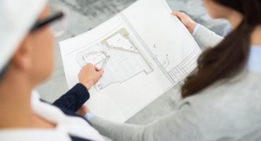 Building designers discussing housing project and viewing blueprint during meeting at construction site