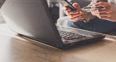 M?n entering secure code on smartphone while shopping online using laptop with bank card.